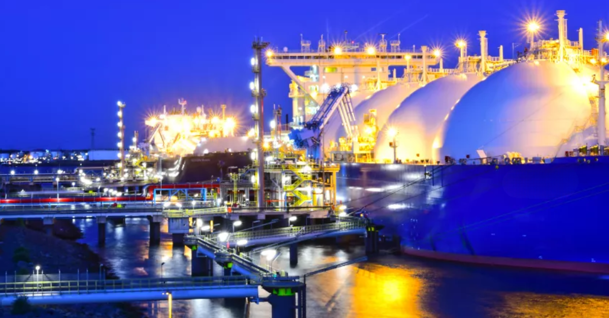 LNG carrier with spherical tanks docked at a brightly lit industrial terminal at night, lights reflecting on the water.